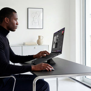 AMP11118 - Slim Fold Laptop Stand | Non-Adhesive | Black LD201-S9 showing side view of person using MacBook laptop propped up on laptop stand and using mouse