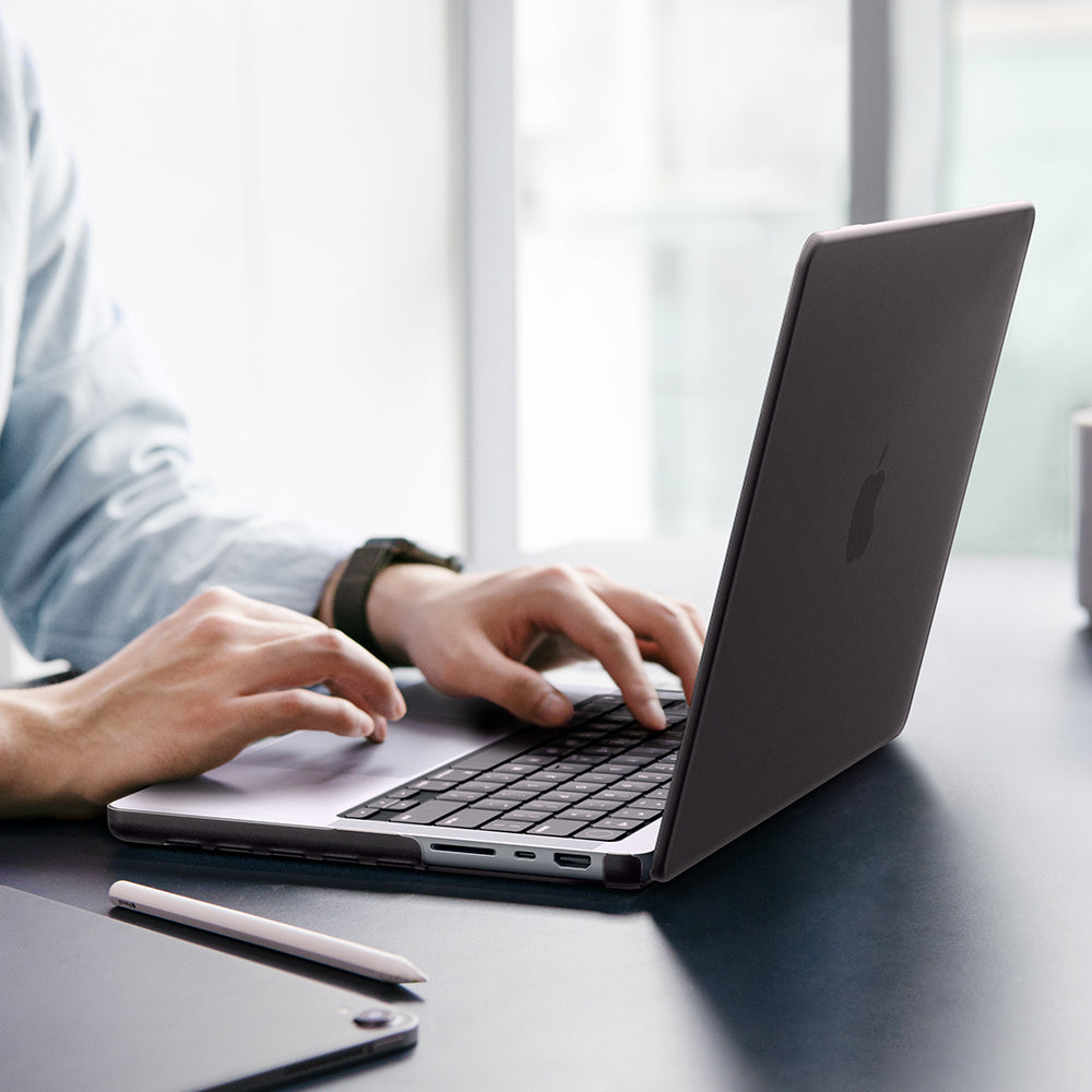 Spigen MacBook Pro 14-inch Air Skin in Frost Black showing a person typing on a MacBook with the Frost Black case applied, placed on a desk in an office setting