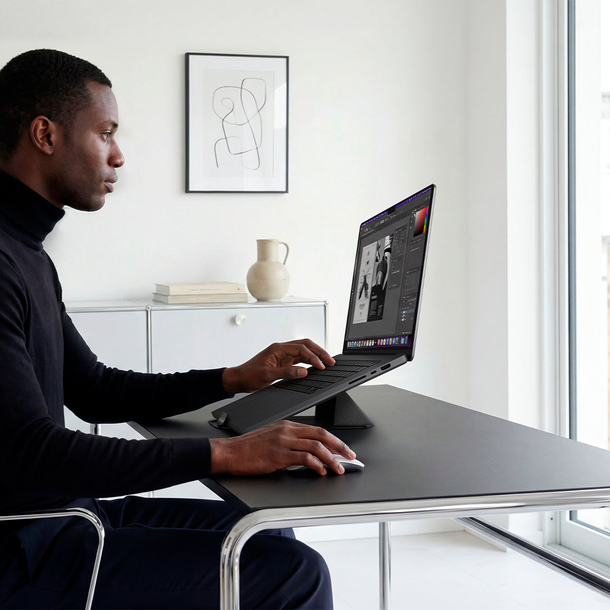 AMP11118 - Slim Fold Laptop Stand | Non-Adhesive | Black LD201-S9 showing side view of person using MacBook laptop propped up on laptop stand and using mouse
